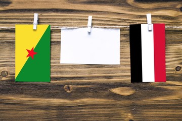 Hanging flags of French Guiana and Yemen attached to rope with clothes pins with copy space on white note paper on wooden background.Diplomatic relations between countries.