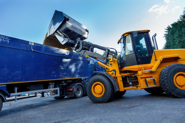 Yellow tractor dumping huge quantities of grain into the back of a articulated lorry