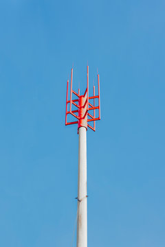 A pole with a red metal tip of several designs against a blue sky - a lightning rod, a lightning rod at the construction site of a house under construction. View from below.