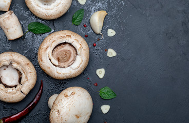 Freshly cut mushrooms (mushrooms, sliced feet, Bisporus agaricus) raw (uncooked), with garlic, chillies, pink pepper, oregano. Black slate background. Space to include texts (copy space)
