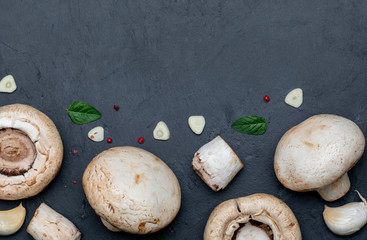 Freshly cut mushrooms (mushrooms, sliced feet, Bisporus agaricus) raw (uncooked), with garlic, chillies, pink pepper, oregano. Black slate background. Space to include texts (copy space)