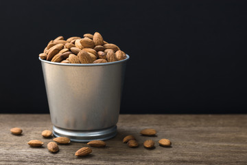 Almonds in stanless bucket on wooden table with copy space.Black background