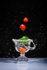 Splashing fruits and vegetables on a crystal glass of water. Fresh strawberries, tomatoes and peppers being shot as they submerged under water on black background.