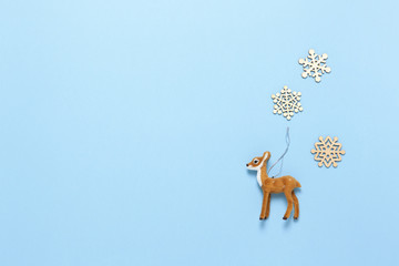 Christmas decoration, naturalistic toy roe deer and three little wooden snowflakes on pastel blue background, copy space. Festive, New Year concept. Horizontal, flat lay. Minimal style. Top view