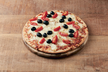 Pizza with mozzarella cheese, cherry tomatoes, black olives and oregano. Home made food. Concept for a tasty and hearty meal. Rustic wooden background. Copy space. 