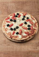 Pizza with mozzarella cheese, cherry tomatoes, black olives and oregano. Home made food. Concept for a tasty and hearty meal. Rustic wooden background. Copy space. 