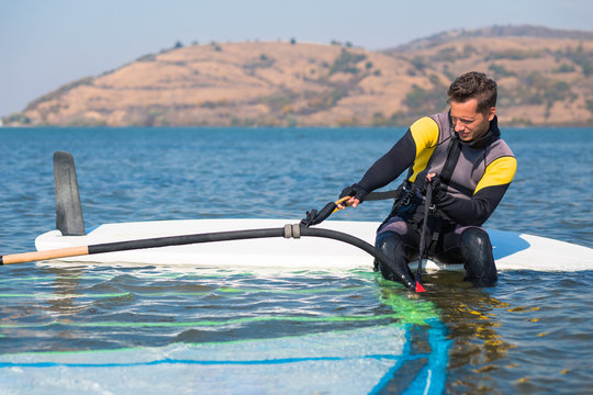 Portrait of windsurfer preparing his equipment while sitting on board.
