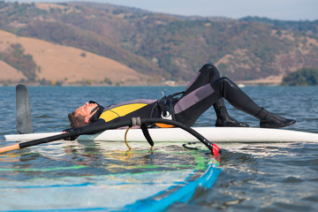 Young windsurfer resting on surfboard in ocean. Sport and recreation concept.