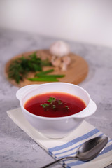 A plate with beetroot borsch on the table, next to the board is parsley, dill, green onions and garlic. Tasty and hearty lunch.