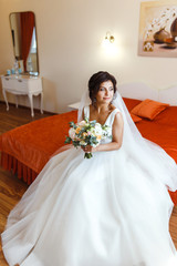 Fototapeta na wymiar Morning of the bride. Beautiful smiling brunette bride in a white dress with a wedding bouquet in her hands. Elegant woman with professional make up and hair style. Wedding morning of the bride. 