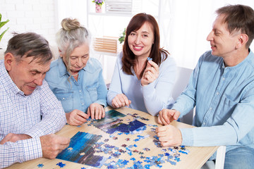 Senior couple and middle age couple solving jigsaw puzzle together with family at home