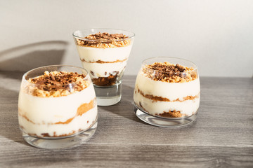 Classic tiramisu dessert in a glass on a gray wooden background. Brightly lit chocolate cake in the amount of three pieces.
