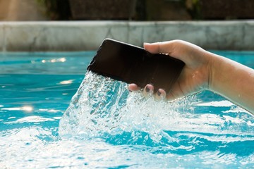 A modern black smartphone makes a splash as it is dropped in the water to test its waterproof...