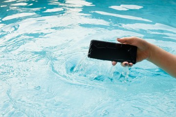 A modern black smartphone makes a splash as it is dropped in the water to test its waterproof construction