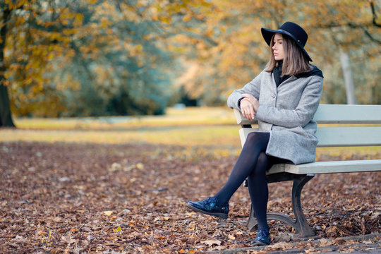Young girl in a hat sitting on a bench in the autumn park
