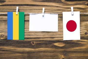 Hanging flags of Gabon and Japan attached to rope with clothes pins with copy space on white note...