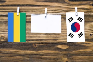 Hanging flags of Gabon and South Korea attached to rope with clothes pins with copy space on white...