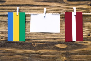 Hanging flags of Gabon and Latvia attached to rope with clothes pins with copy space on white note...