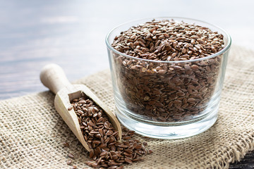 Fresh organic flax seeds in a glass bowl on sackcloth background. Ingredients for healthy eating.