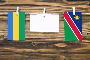 Hanging flags of Gabon and Namibia attached to rope with clothes pins with copy space on white note paper on wooden background.Diplomatic relations between countries.