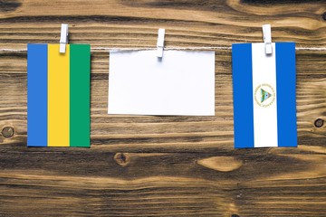 Hanging flags of Gabon and Nicaragua attached to rope with clothes pins with copy space on white note paper on wooden background.Diplomatic relations between countries.