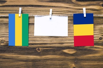 Hanging flags of Gabon and Romania attached to rope with clothes pins with copy space on white note...