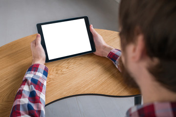 Mockup image: over shoulder close up view of man looking at modern digital tablet computer device with white blank screen. Mock up, copyspace, leisure time, template and technology concept