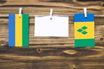 Hanging flags of Gabon and Saint Vincent And The Grenadines attached to rope with clothes pins with copy space on white note paper on wooden background.Diplomatic relations between countries.