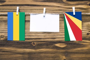 Hanging flags of Gabon and Seychelles attached to rope with clothes pins with copy space on white...