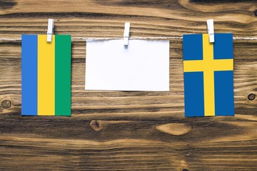 Hanging flags of Gabon and Sweden attached to rope with clothes pins with copy space on white note...