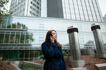 Young businesswoman speaking on mobile phone during outdoor coffee break, near office building. Frankfurt, Germany. Communication concept