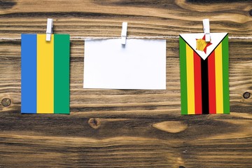 Hanging flags of Gabon and Zimbabwe attached to rope with clothes pins with copy space on white...