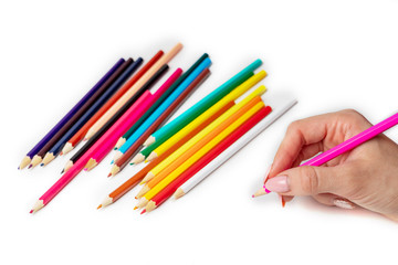hand holds the colored pencil, in the background a lot of colored pencils