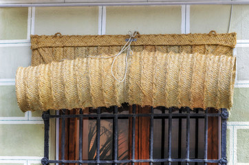 Esparto shutter, rolled up, in the outside of a window with black bars. Handcrafted product to protect the house of the sunlight and high temperatures.
