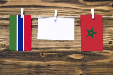 Hanging flags of Gambia and Morocco attached to rope with clothes pins with copy space on white note paper on wooden background.Diplomatic relations between countries.