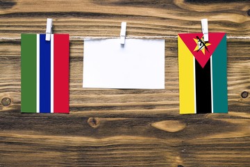 Hanging flags of Gambia and Mozambique attached to rope with clothes pins with copy space on white...