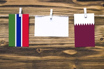 Hanging flags of Gambia and Qatar attached to rope with clothes pins with copy space on white note...