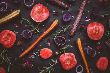 Fruit and vegetable collage on black background: red moon apples, onion rings, purple haze carrots, rosemary