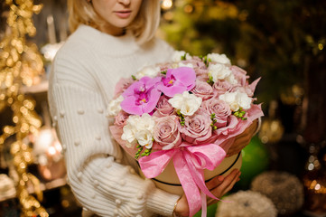 Young woman holding a box of pink roses and orchids decorated with white jasmine