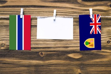 Hanging flags of Gambia and Turks And Caicos Islands attached to rope with clothes pins with copy space on white note paper on wooden background.Diplomatic relations between countries.