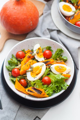 Lunch bowl with cherry tomatoes, roasted pumpkin, green salad, seeds and boiled eggs. Grey plate on white background. 