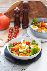Lunch bowl with cherry tomatoes, roasted pumpkin, green salad, seeds and boiled eggs. Grey plate on white background. 