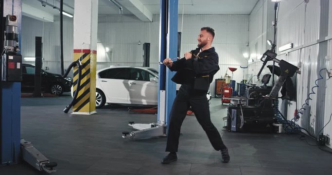 Modern service auto mechanic guy dancing very excited in front of the camera while he fixing the car