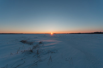 Sun rising over ice fields covering a river in winter in river delta of Kokemäenjoki in Pori,...