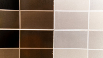 A square shaped tile wall in the toilet with a black brown and white color.