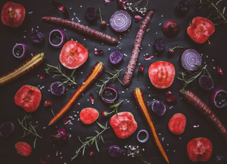 Fruit and vegetable collage on black background: red moon apples, purple haze carrots, onion rings, rosemary
