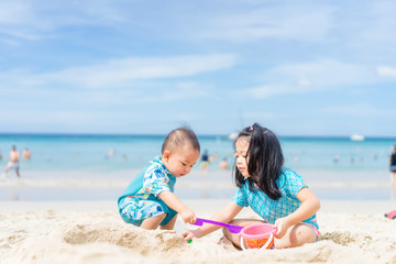 4 years old Little asian girl playing on the beach with her 1 year old baby brother.Children in nature with beautiful sea, sand and blue sky.Happy kids on vacations at seaside Sibling on Vacation.