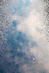 reflection of the blue sky with clouds in a puddle on the pavement