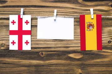 Hanging flags of Georgia and Spain attached to rope with clothes pins with copy space on white note paper on wooden background.Diplomatic relations between countries.