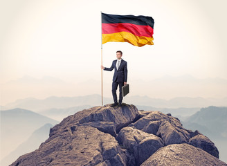 Successful businessman on the top of a mountain holding victory flag